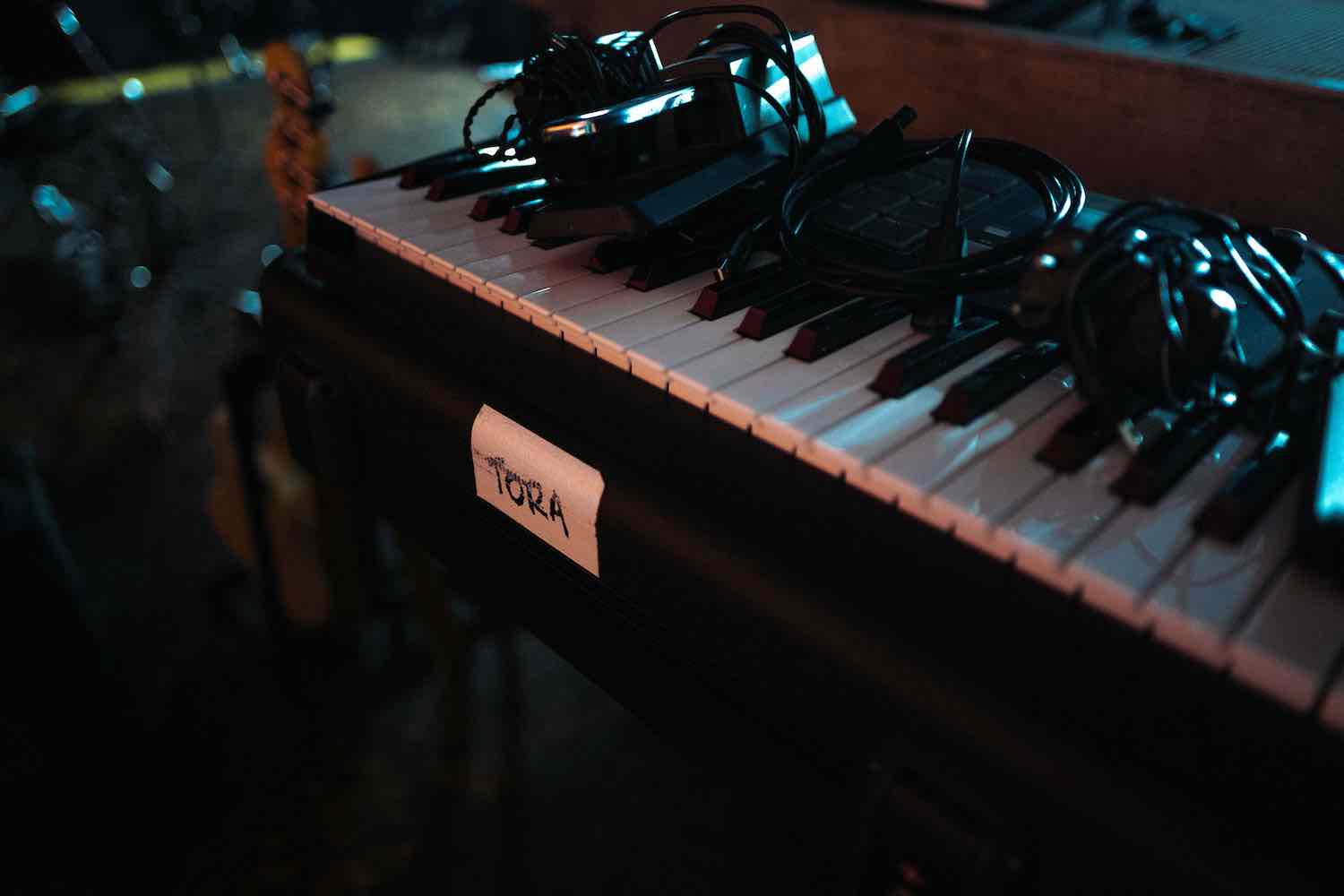 Close-up of a vintage analogue synthesiser in low light, a TORA sticker on its casing