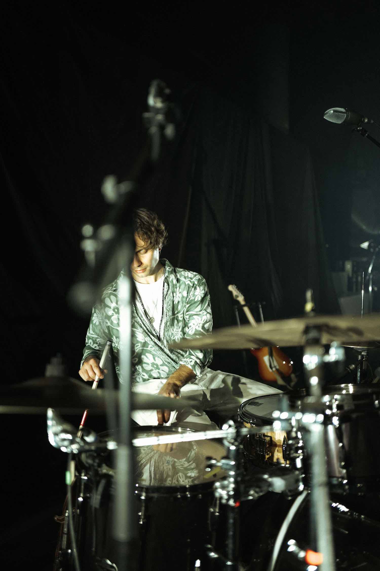 A member of the band playing drums on a dark stage