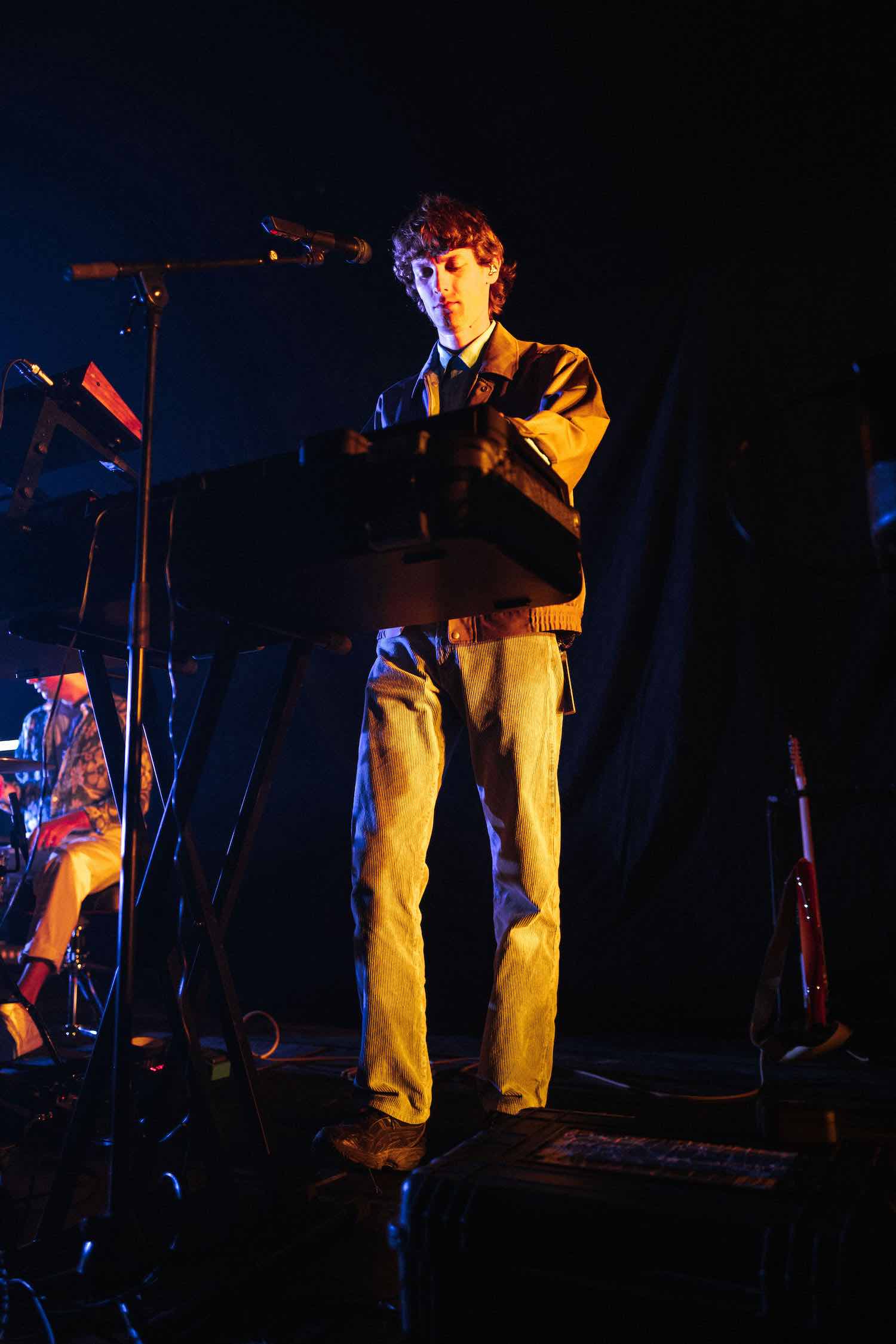 A member singing behind a keyboard, lit blue from the side