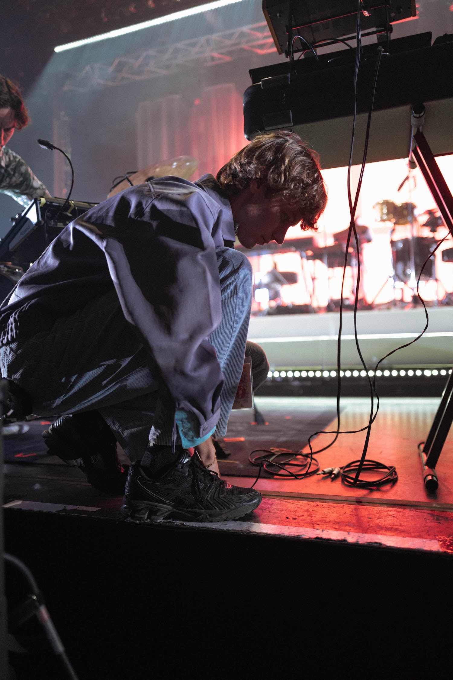 A member leaning over equipment at the front of a red-lit stage