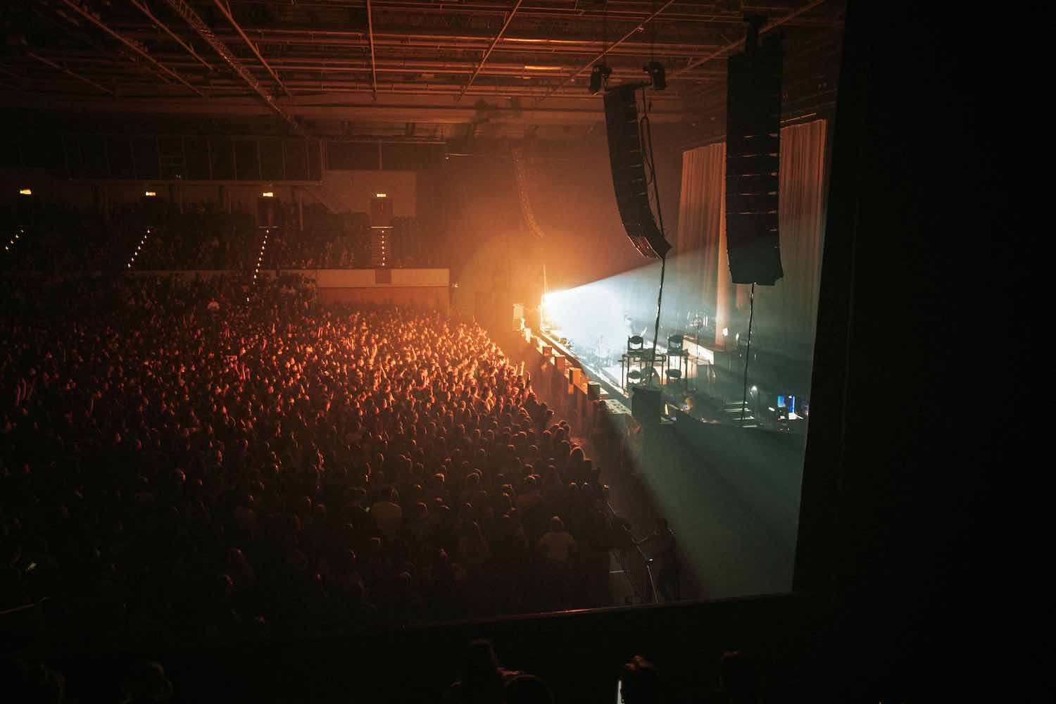 A packed concert crowd seen from the side of the stage