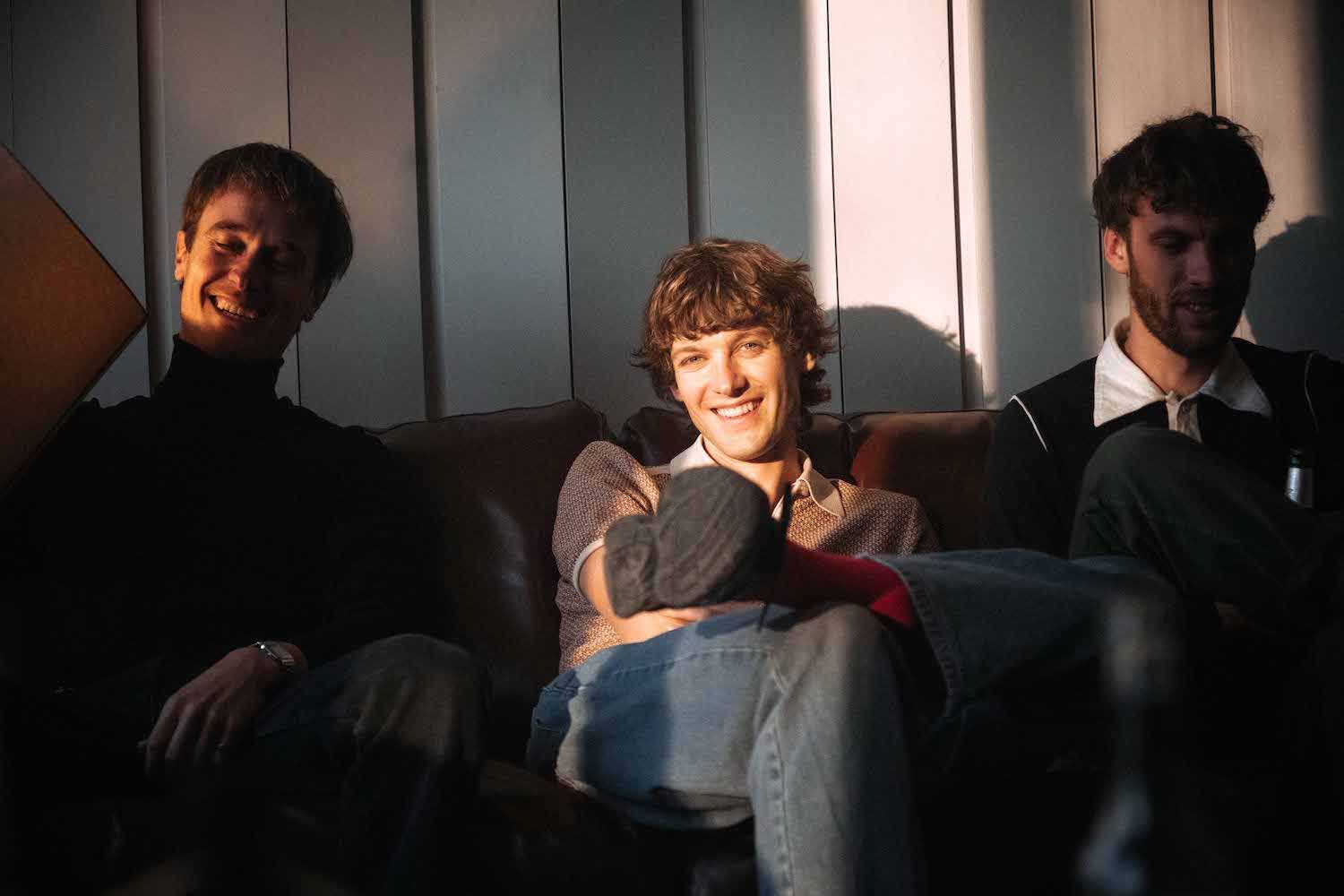 Three members of the band sitting and laughing together on a sofa