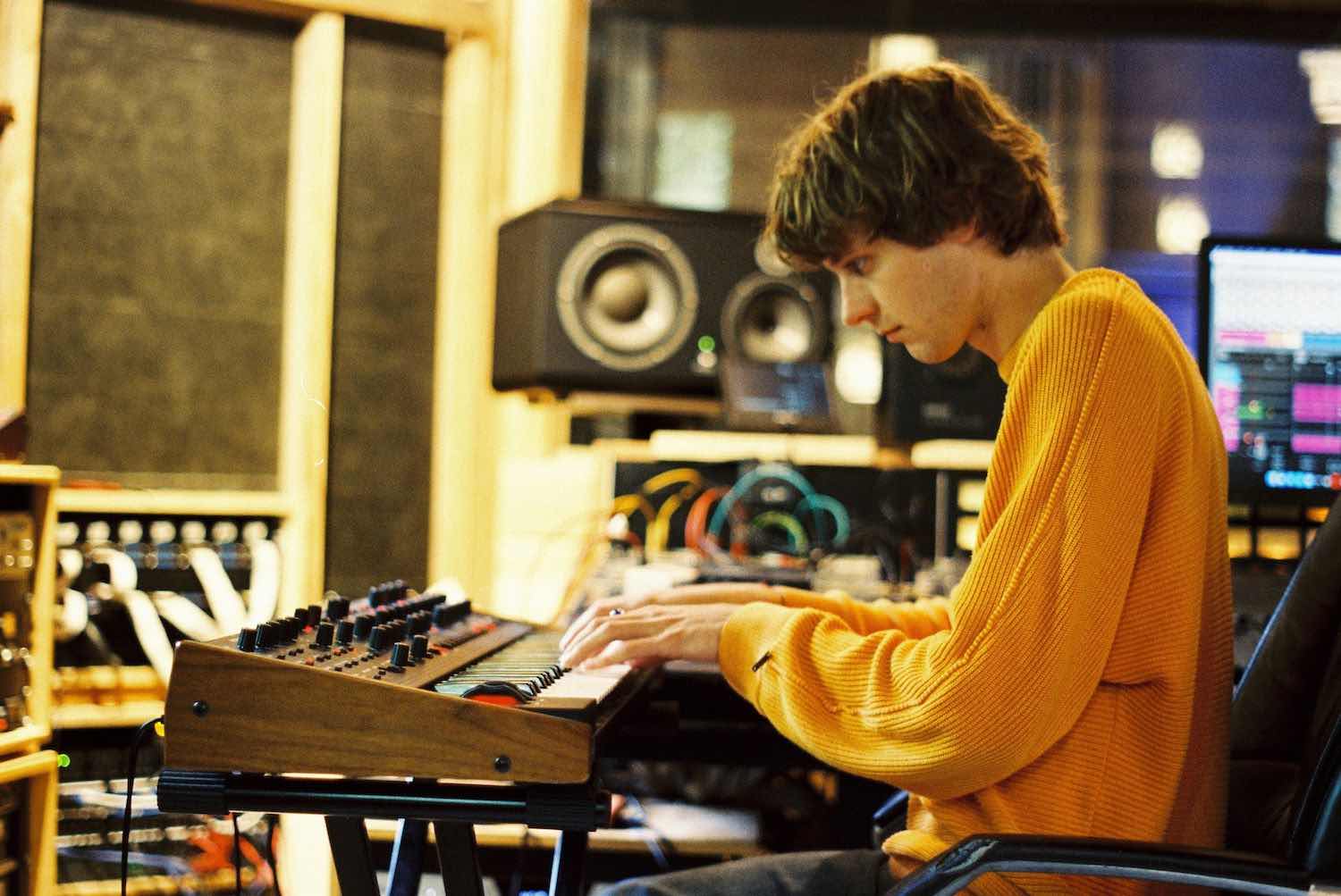 A member in an orange jumper playing a synthesiser in the studio