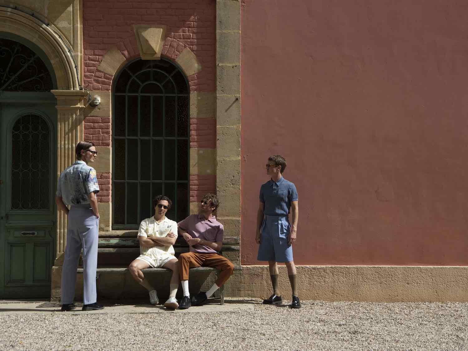 The band outside a brick and pink stucco building, one seated on the step