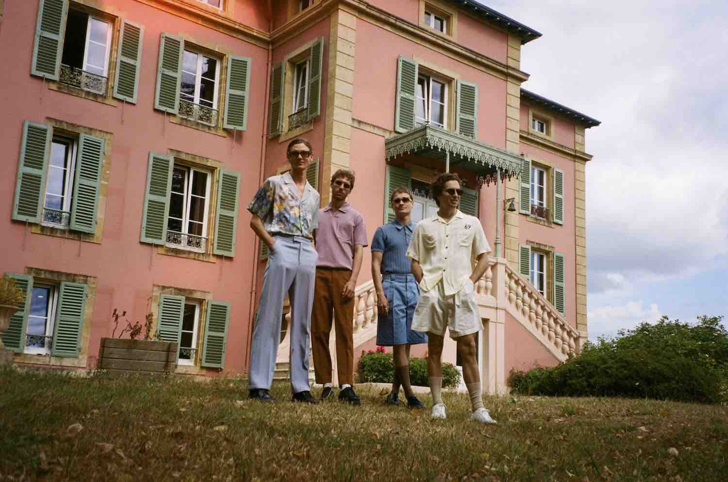 The band on the lawn in front of a large pink villa with green shutters